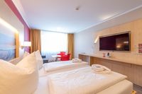 Ein Doppelzimmer mit zwei Betten und zwei roten Sesseln bereitgestellt vom Hotel an der Stadthalle in Rostock